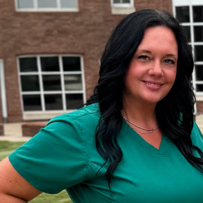 Graduate stands in scrubs in front of OHIO Southern brick building
