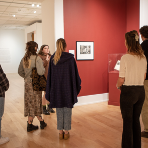 students stand in a red walled gallery looking at framed art in the Kennedy Museum 