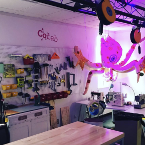 a workroom filled with tools hanging on the wall, a work table, with a plush octopus that hangs from the ceiling with a purple light glowing behind it