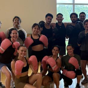 group of boxing students smile at the camera with boxing gloves in their hands