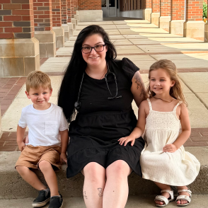 Graduate seated on steps with young children at her side