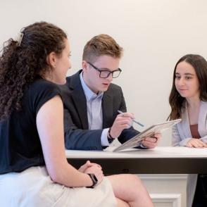 students sit at a desk discussing and pointing at a tablet screen