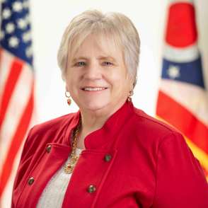 Headshot of Jennifer Lloyd in front of Ohio and American flags, wearing red jacket