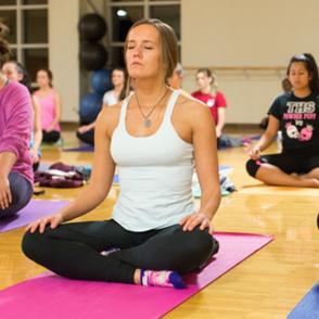 students practice mindfulness in group yoga class sitting with their eyes closed