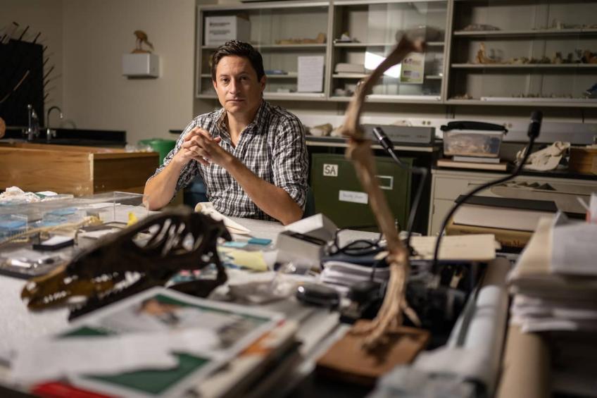 Faculty researcher Patrick O'Connor poses at his desk surrounded by paperwork and dinosaur bones