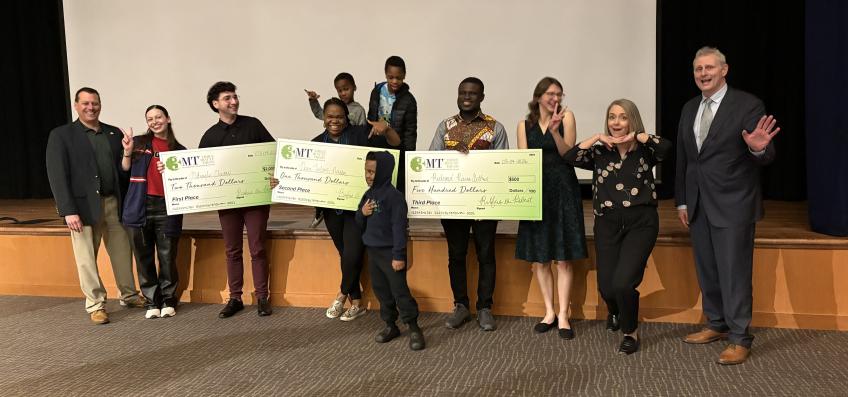 A group of people standing in front of a stage, three holding large checks