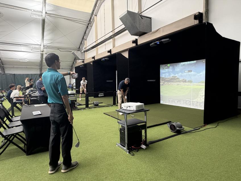 person waits in line as another person takes a shot with their golf club at the golf simulator in the background