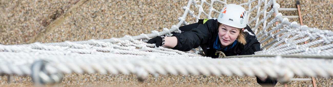 A student climbs a rope net in a challenge course