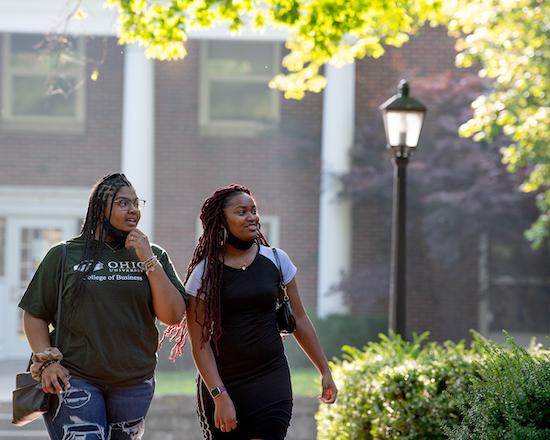 Two Ohio University students walk together on College Green in early spring
