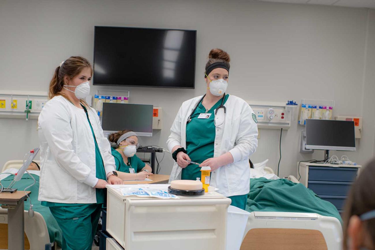 Two nursing students at a medical cart in front of two patient beds