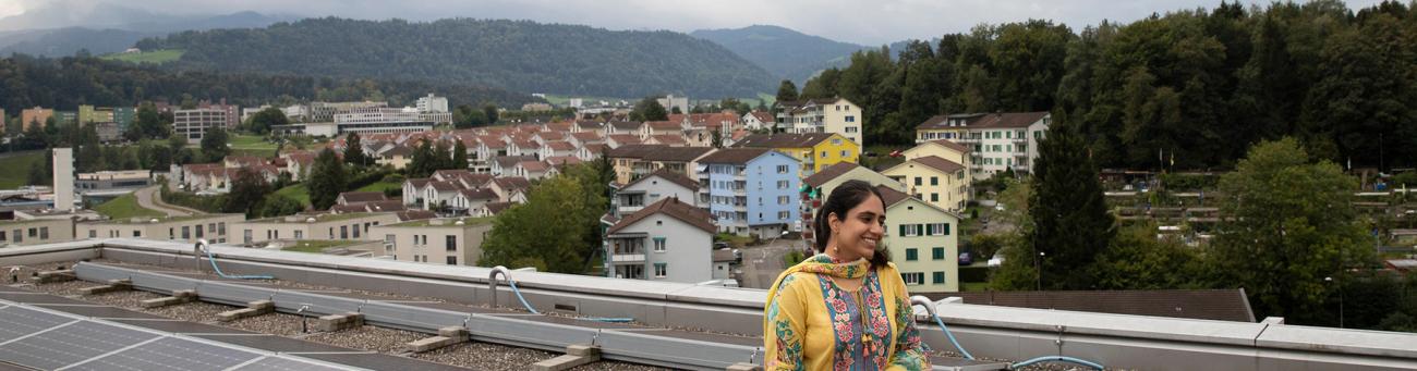 Ohio University student stands on balcony in Switzerland with mountains and buildings in the background