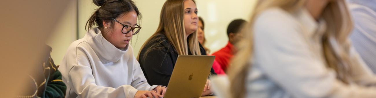 A student works on a laptop during class surrounded by other students