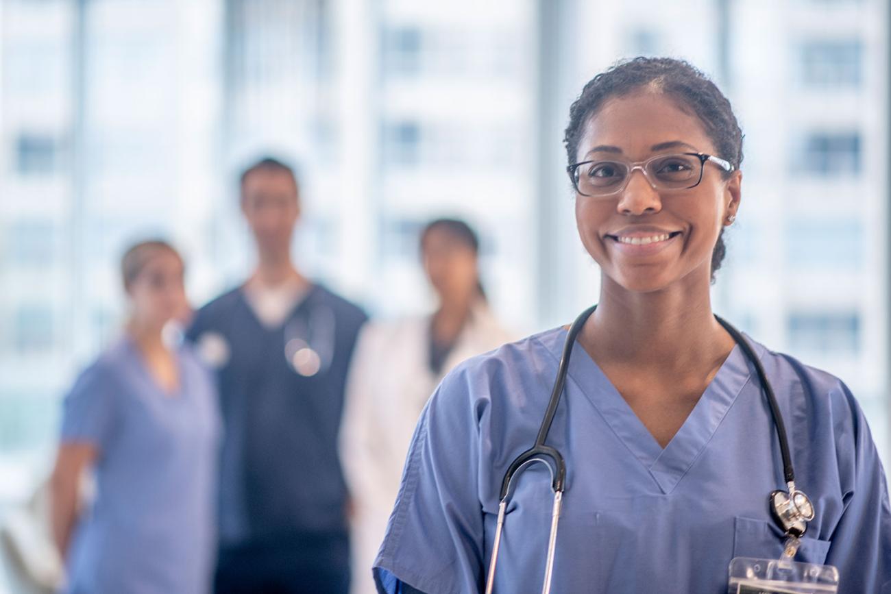 Smiling woman in blue scrubs in foreground with blurred images of others in background