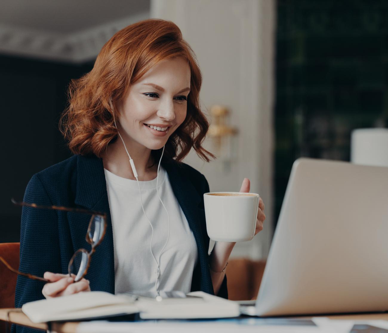 A woman sitting at a computer holding eyeglasses and a coffee mug