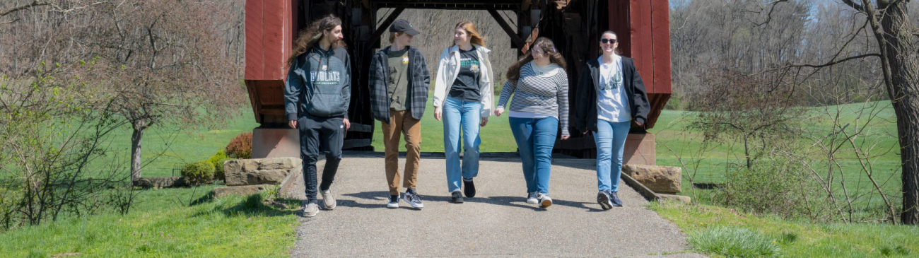 Group of people from Lancaster campus on a walk together with covered bridge behind them.