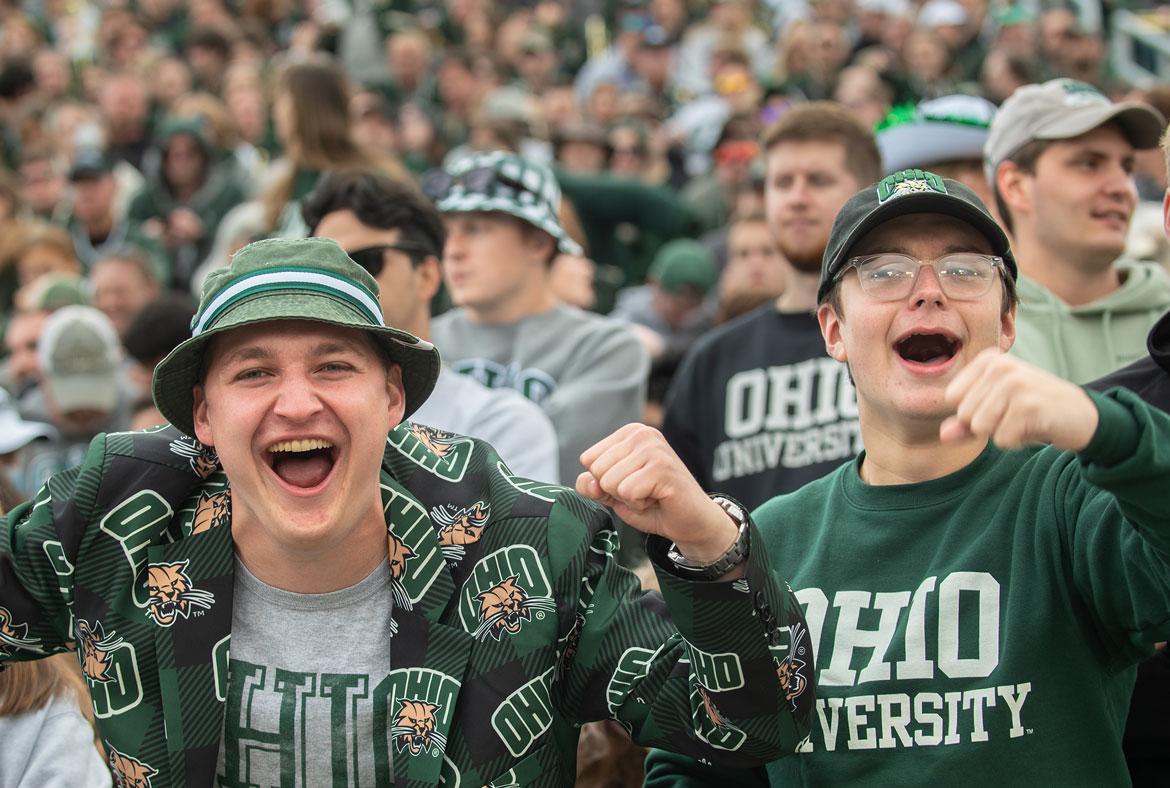 Two students wearing OHIO gear cheer at an OHIO football game.