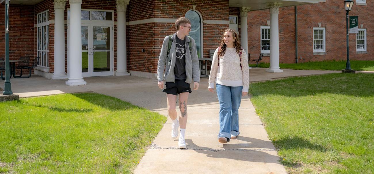 Two students walk through campus and talk.