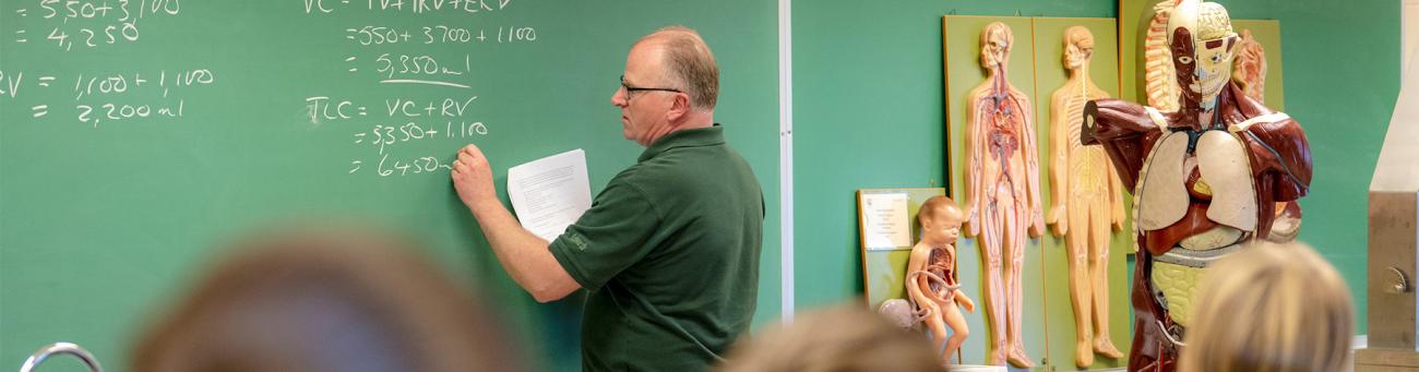 A professor writes on a chalkboard during class.