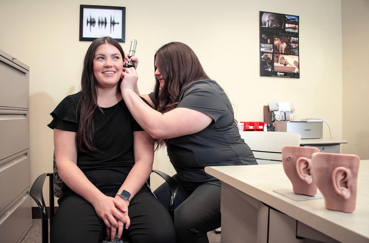 A student examines a patient's ears in a hearing, speech and language clinic