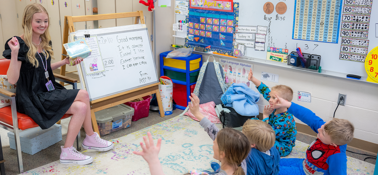 Young teacher sits at front of classroom while primary students sit on rug