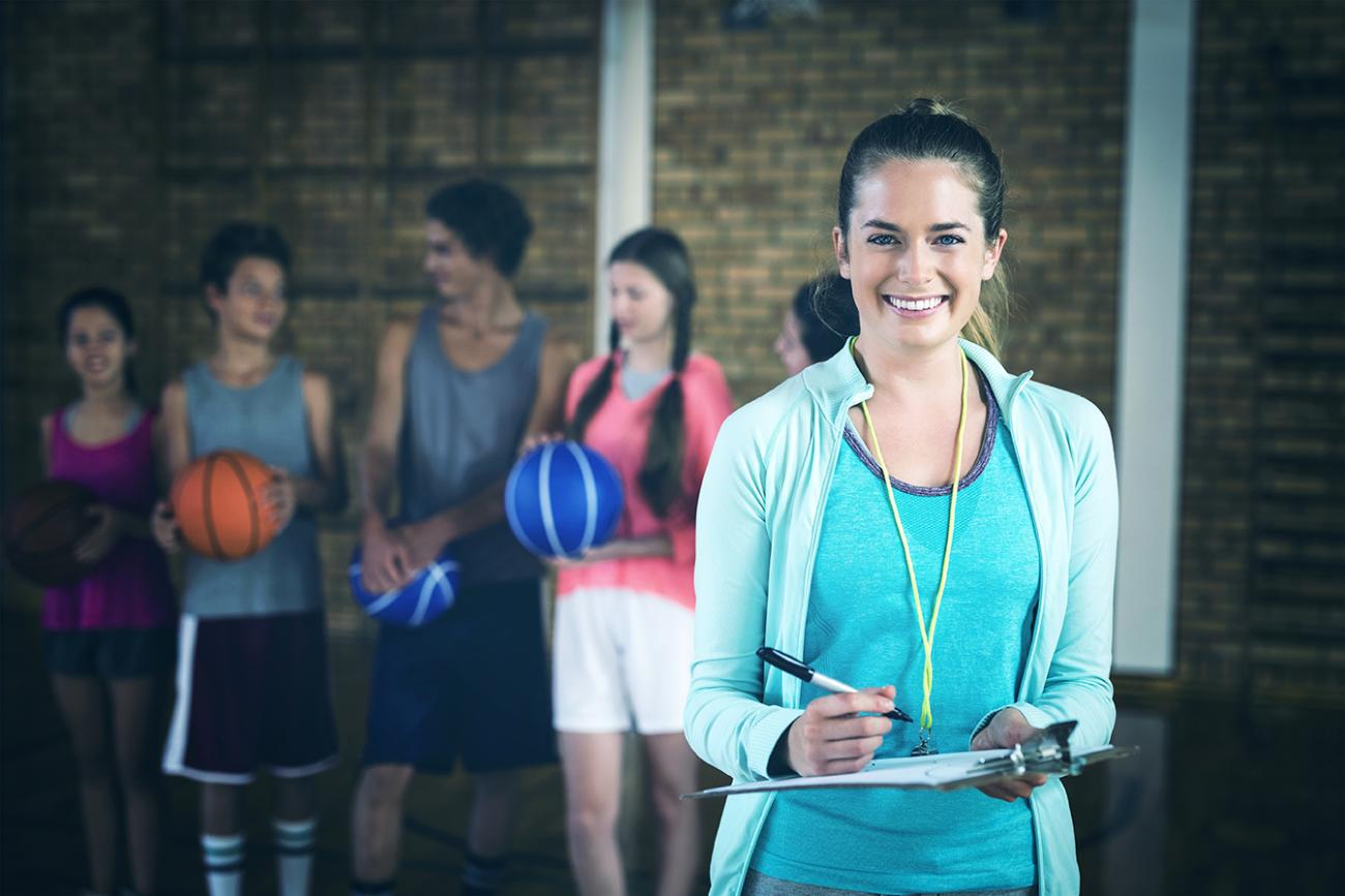 Woman (coach) holding a clipboard with basketball team sitting on bench behind her