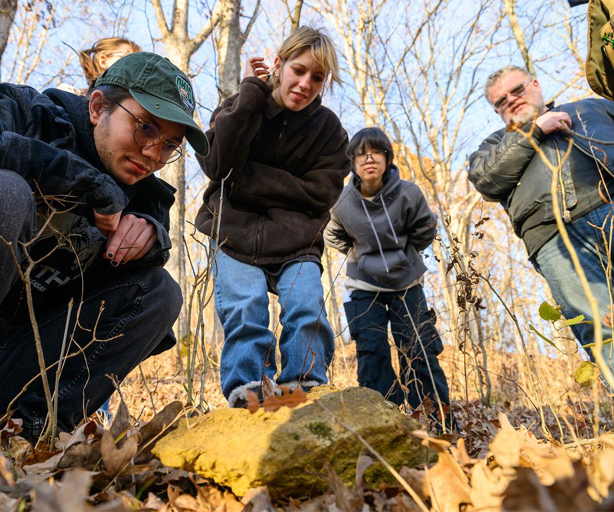 A group of students crouch near the ground to inspect the ground in a plant biology class.