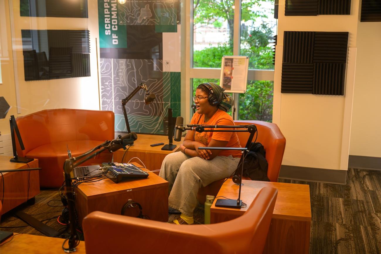 woman sits in a room with multiple microphones setup for podcasting