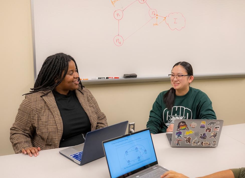 Two women sitting at a desk with laptops in front of them
