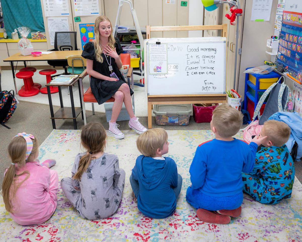 5 young children sitting on the floor of a classroom listening to teacher