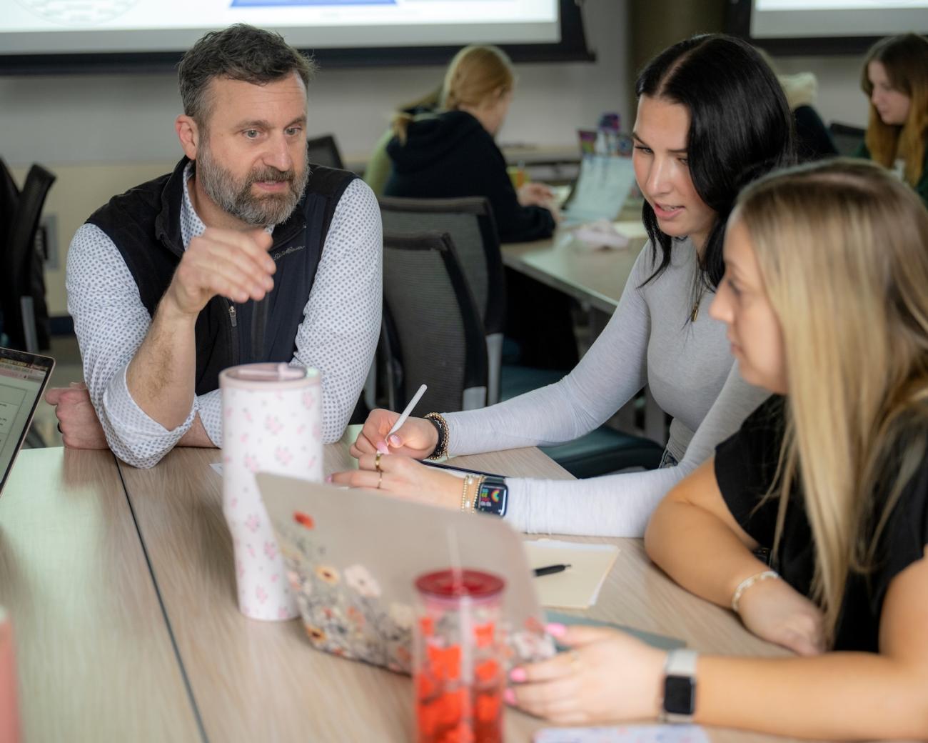 teacher talking to students and looking at a laptop