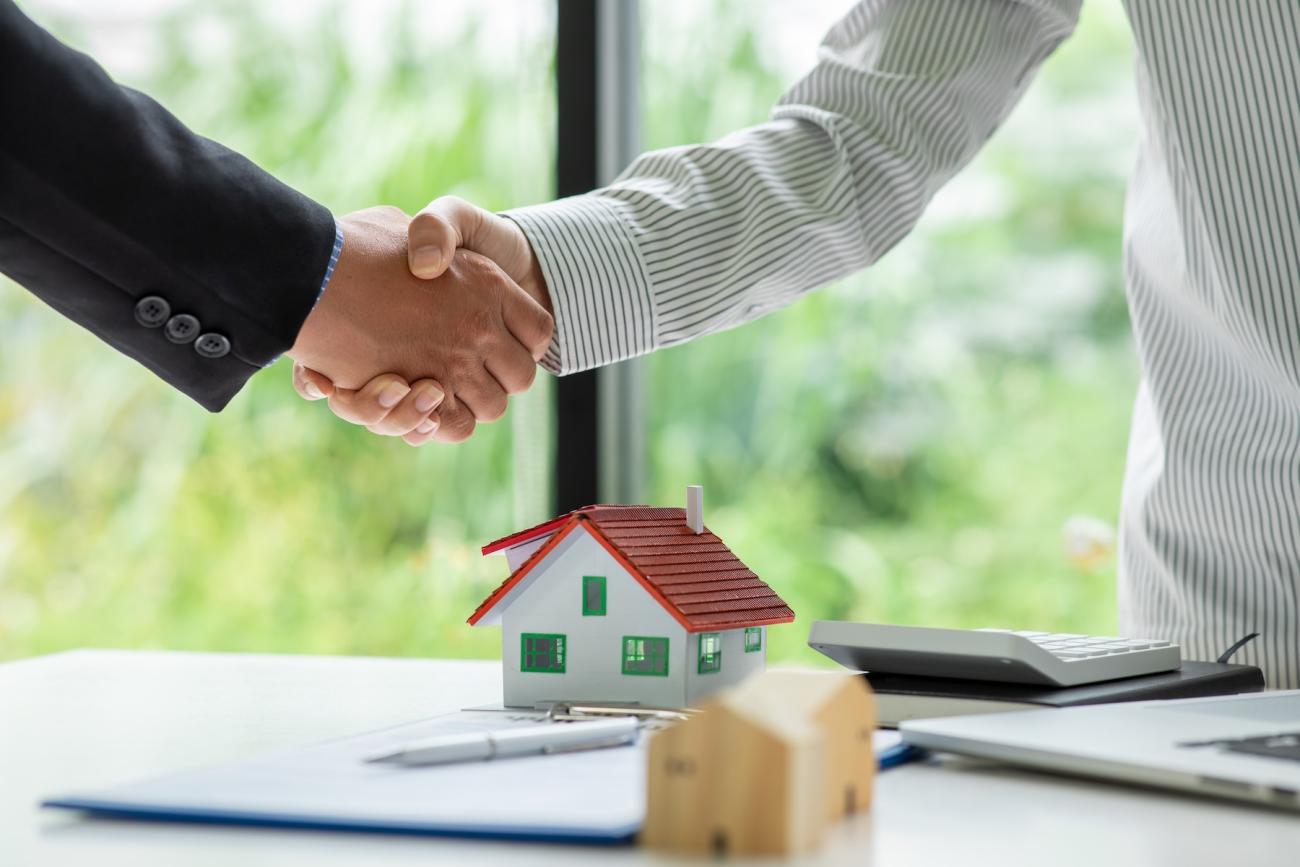 two people shaking hands over a desk with a model home