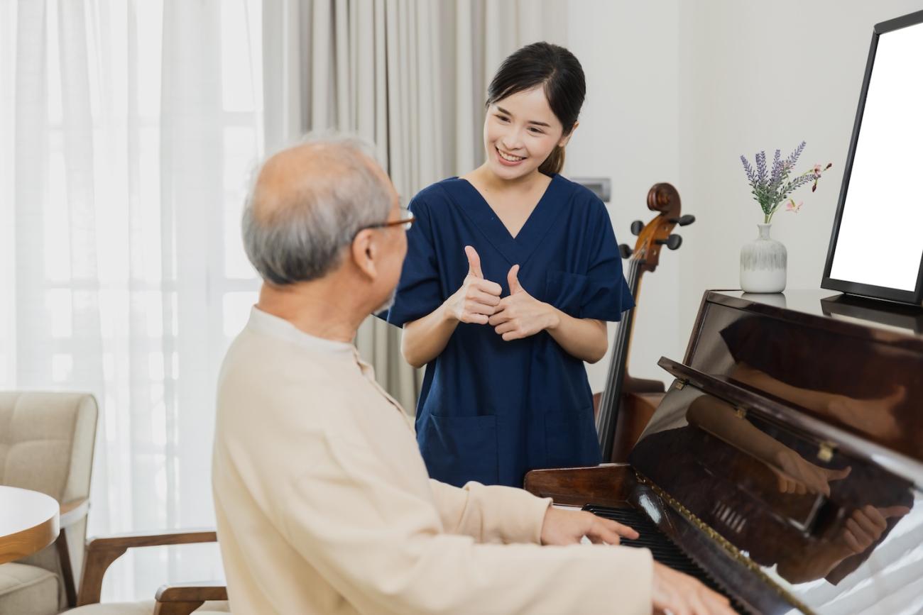 Nurse giving a "thumbs up" to elderly man playing piano