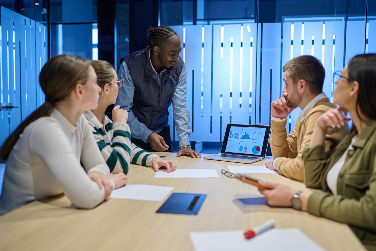 group of 5 people in a meeting room looking at graphs on a small screen