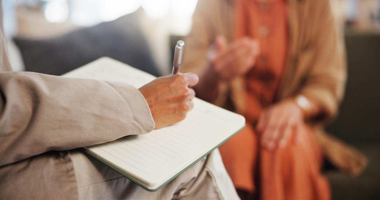woman writes in a notebook while someone talks in therapy