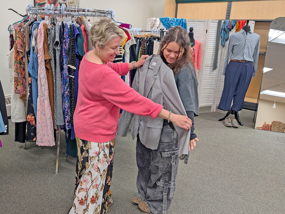 Woman holds suit jacket up against student, gauging size
