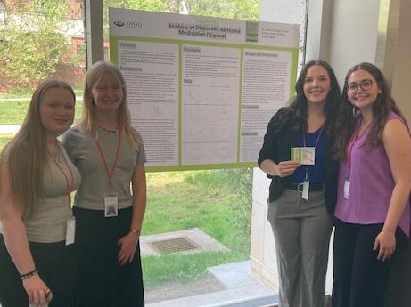 Chemistry students stand beside their informational presentation on medication disposal.