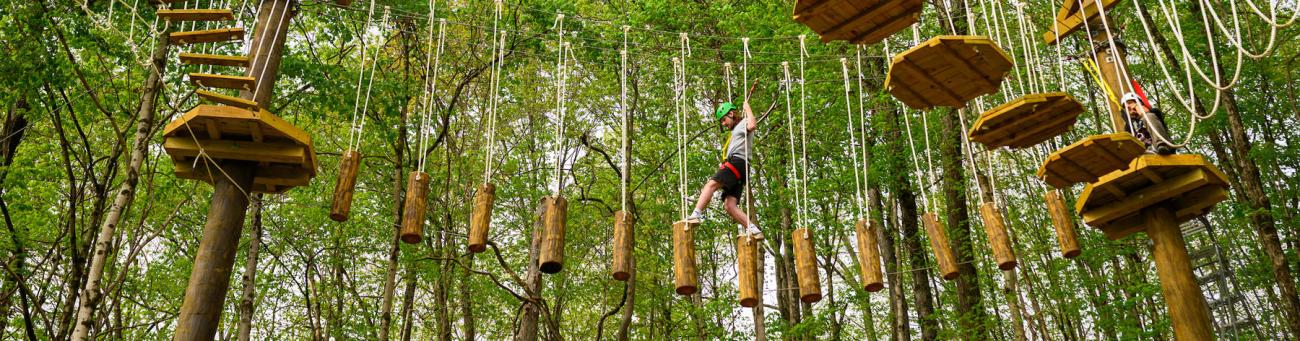 man carefully climbs the challenge course obstacles against beautiful green background of trees
