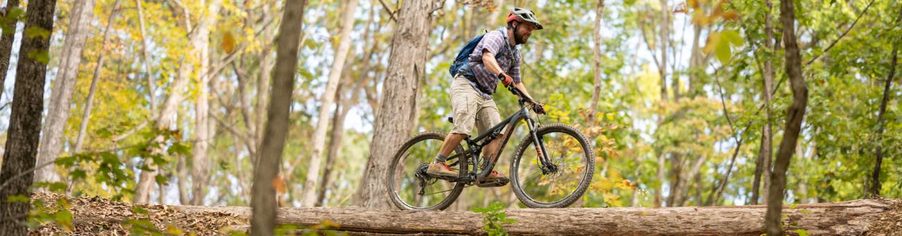 man rides bike on fallen tree bark with beautiful green forest background