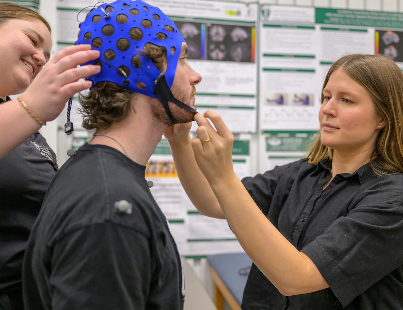 Two students apply a special helmet on a patient for testing.
