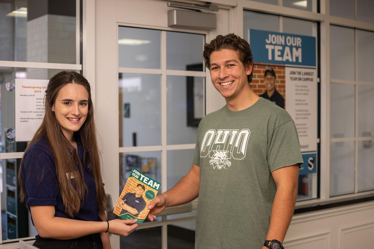 student employee handing a team brochure to another student