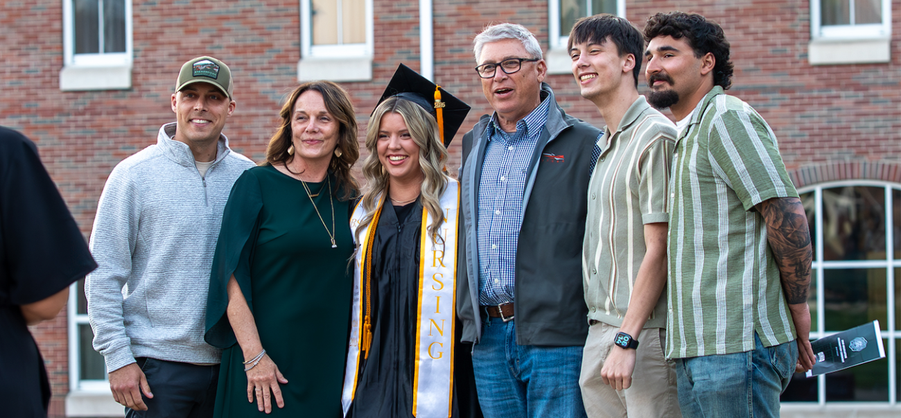 Graduate in cap and gown standing with family in front of Ohio University Southern's Vern Riffe Center