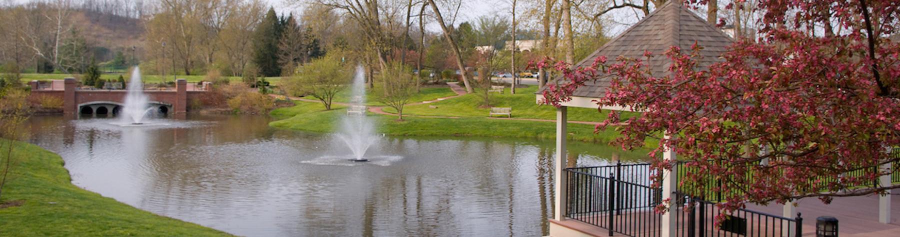 Overlooking fountains in a lake and a gazebo in the distance surrounded by foliage.