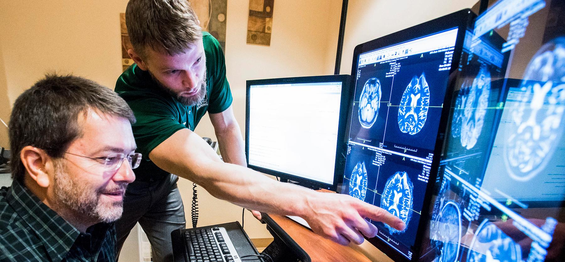 A student points at a computer image of a brain, working on research with a professor
