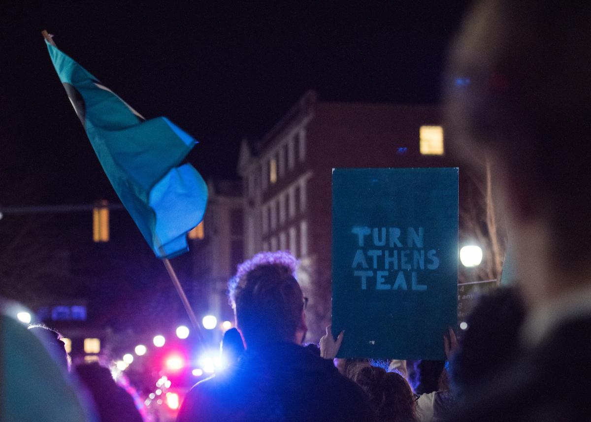 A marcher holds up a sign that reads "Turn Athens Teal," in reference to the official color for supporting survivors