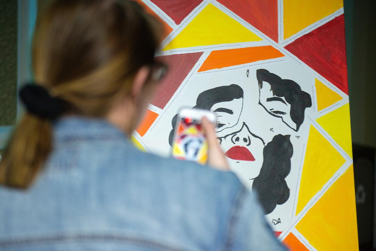 A participant takes a photo of an art piece on display at the event, featured fragmented pieces of a face
