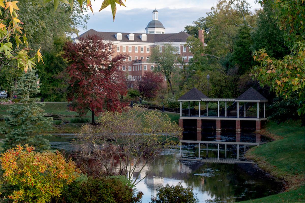 Emeriti Park at Ohio University, featuring fall foliage surrounding a small pond on campus, with a brick building in the background