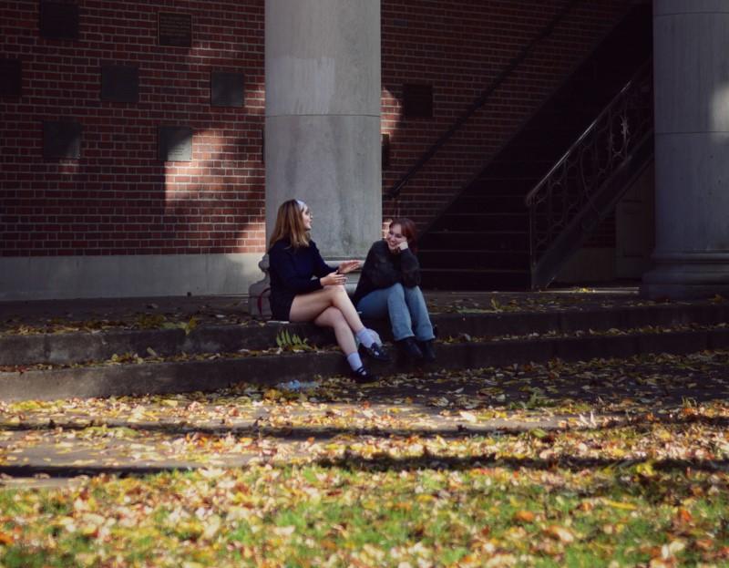 Templeton-Blackburn Alumni Memorial Auditorium: Two girls are chatting and enjoying autumn on campus, sunlight shines down with falling leaves.
