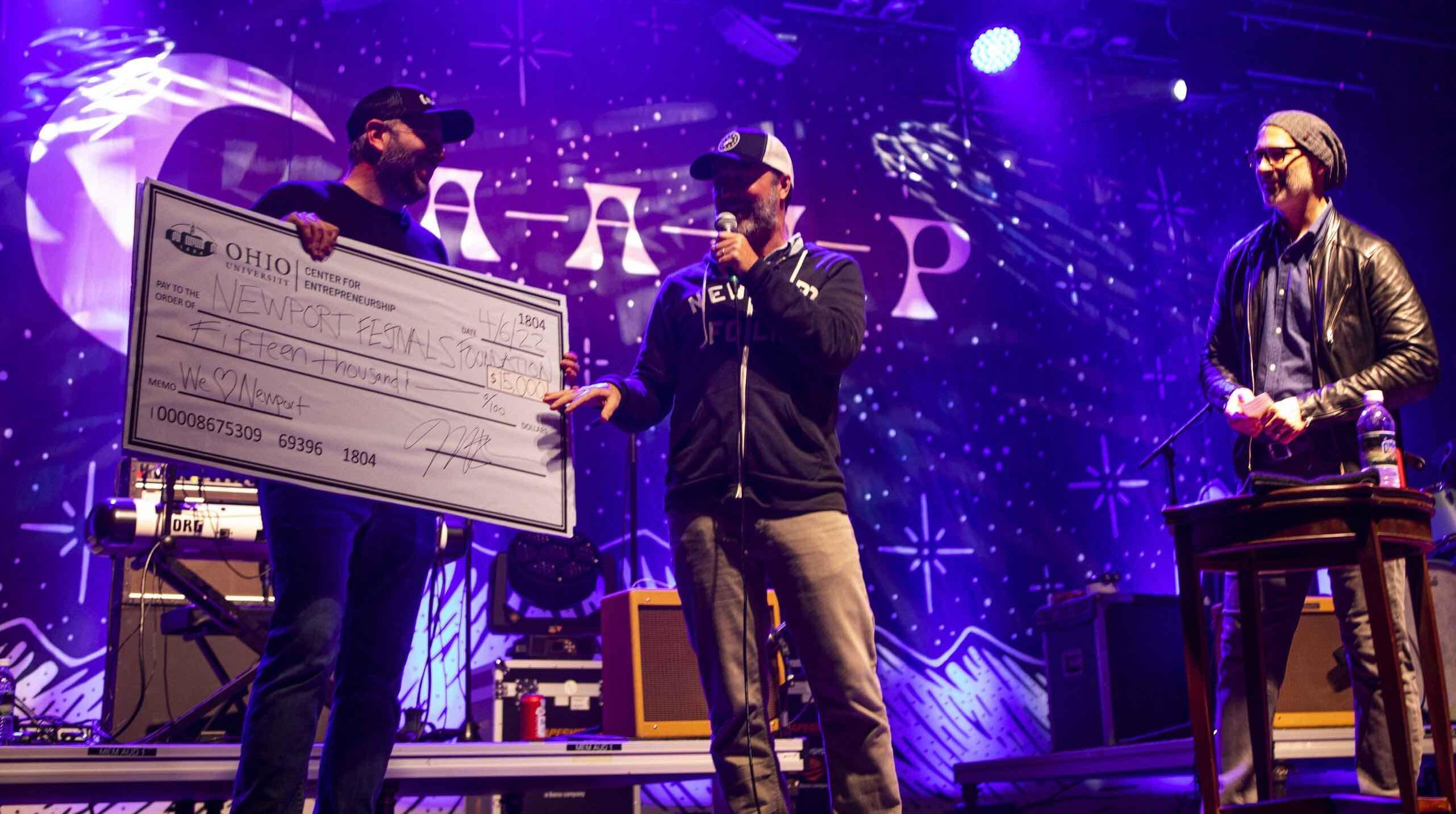 Three men on stage presenting an oversized check donation