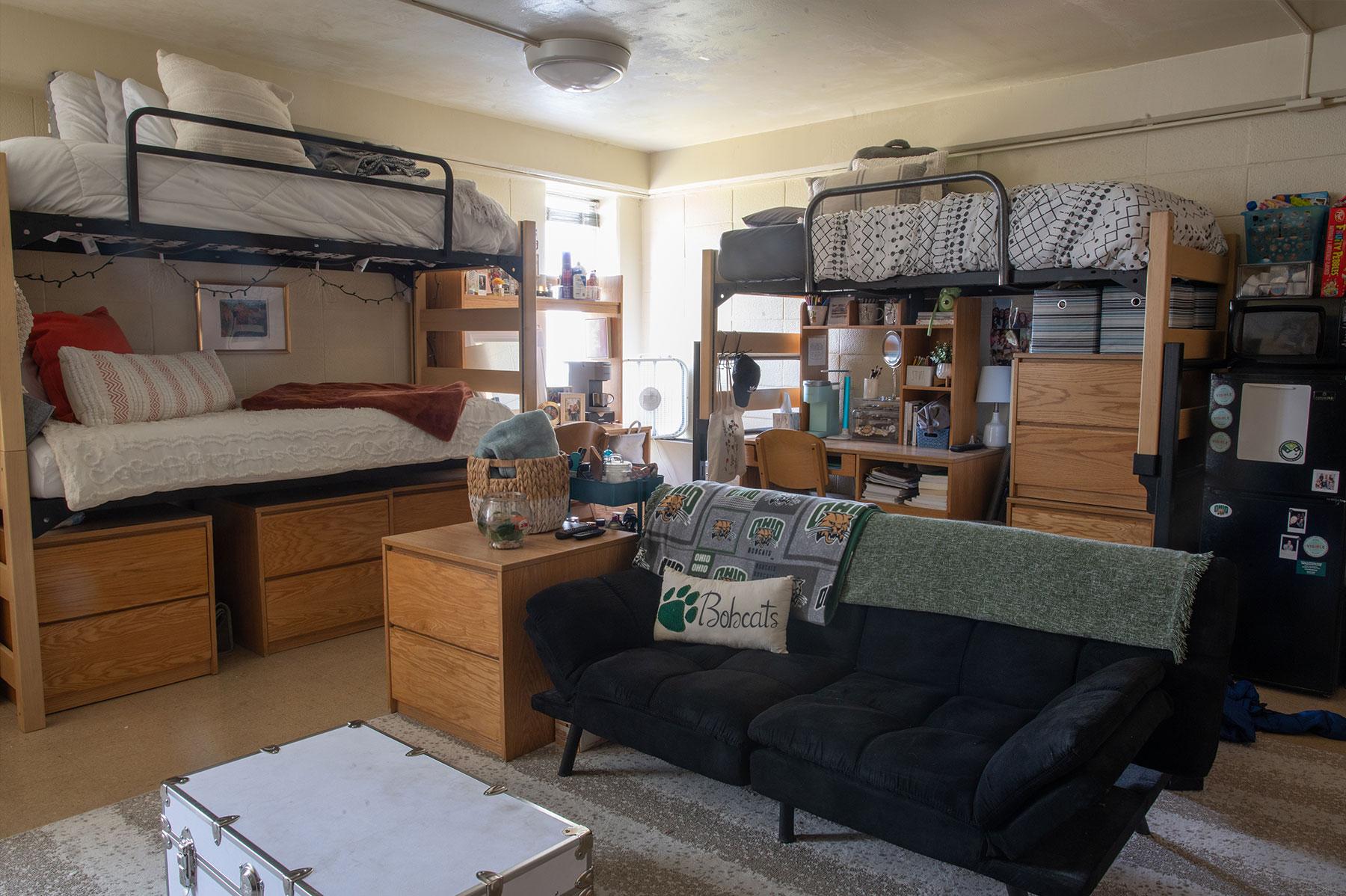 Inside a residence hall room in OHIO's Convocation Center, showing lofted beds, a couch with a makeshift coffee table, and desks with storage drawers