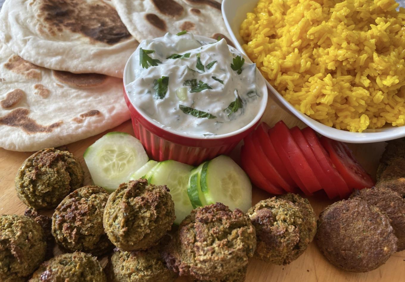 Platter holding pita bread, tzatzikii sauce, lemon rice, fresh veggies and falafel.